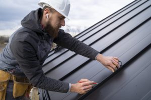 Мужчина кровельщик обшивает крышу дома профнастилом